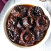Stewed prunes are served in a white bowl with a napkin and a spoon.