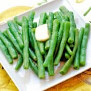 Boiled green beans served on a white plate, topped with butter.