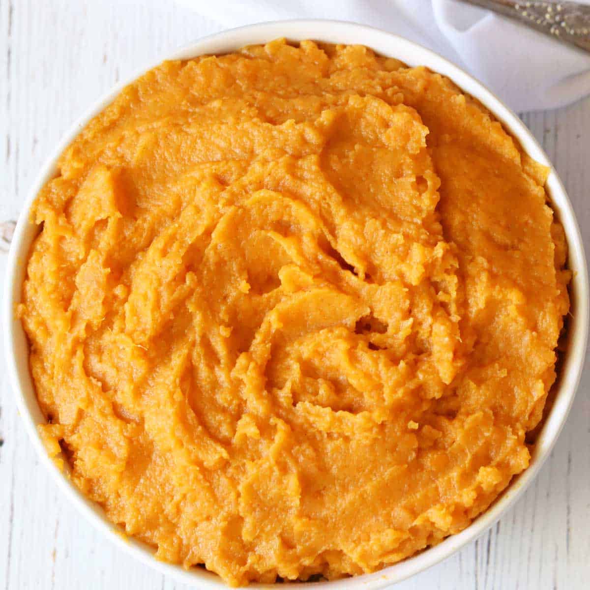Mashed sweet potatoes are served in a white bowl.