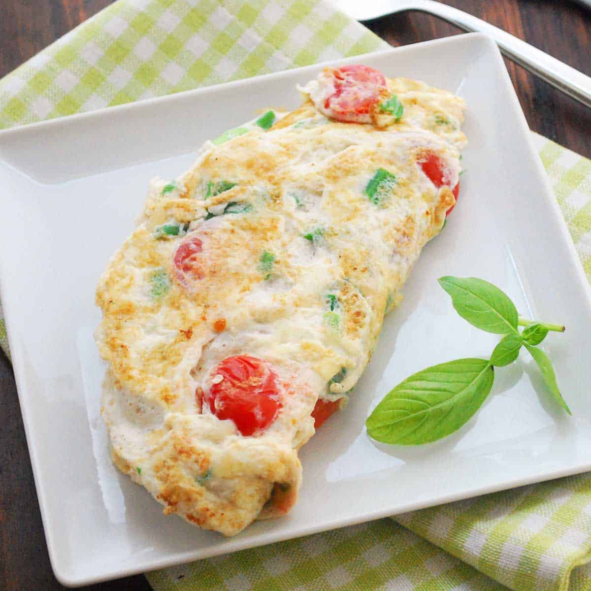 Egg white omelet served on a white plate with basil for garnish.