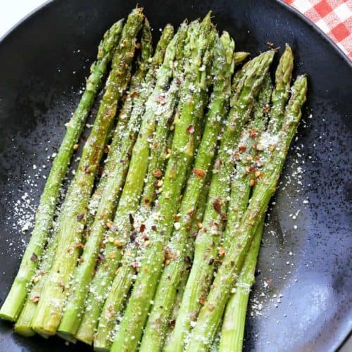 Roasted asparagus topped with Parmesan and served on a dark plate.