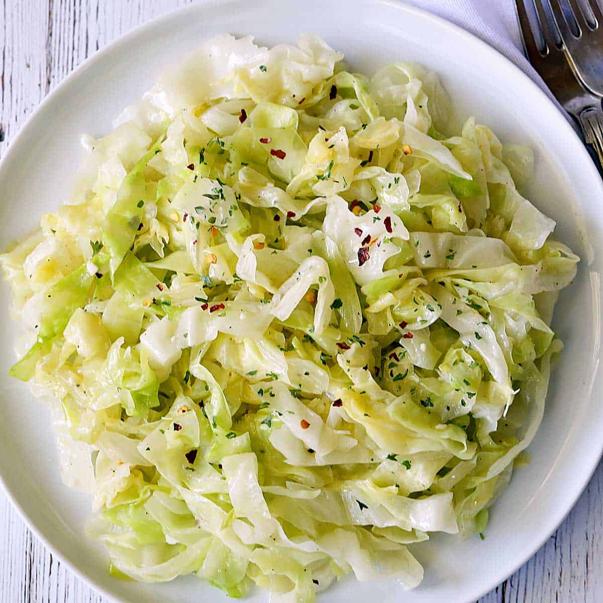 Steamed cabbage is served on a white plate with forks and a napkin.