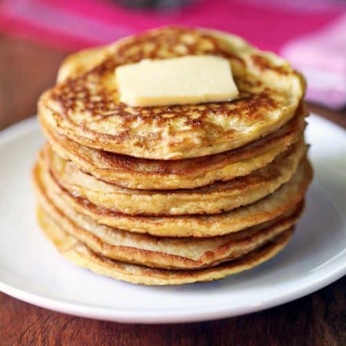 Coconut flour pancakes stacked on a white plate and topped with butter.