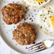 Sausage patties are served on a white plate with eggs and a fork.