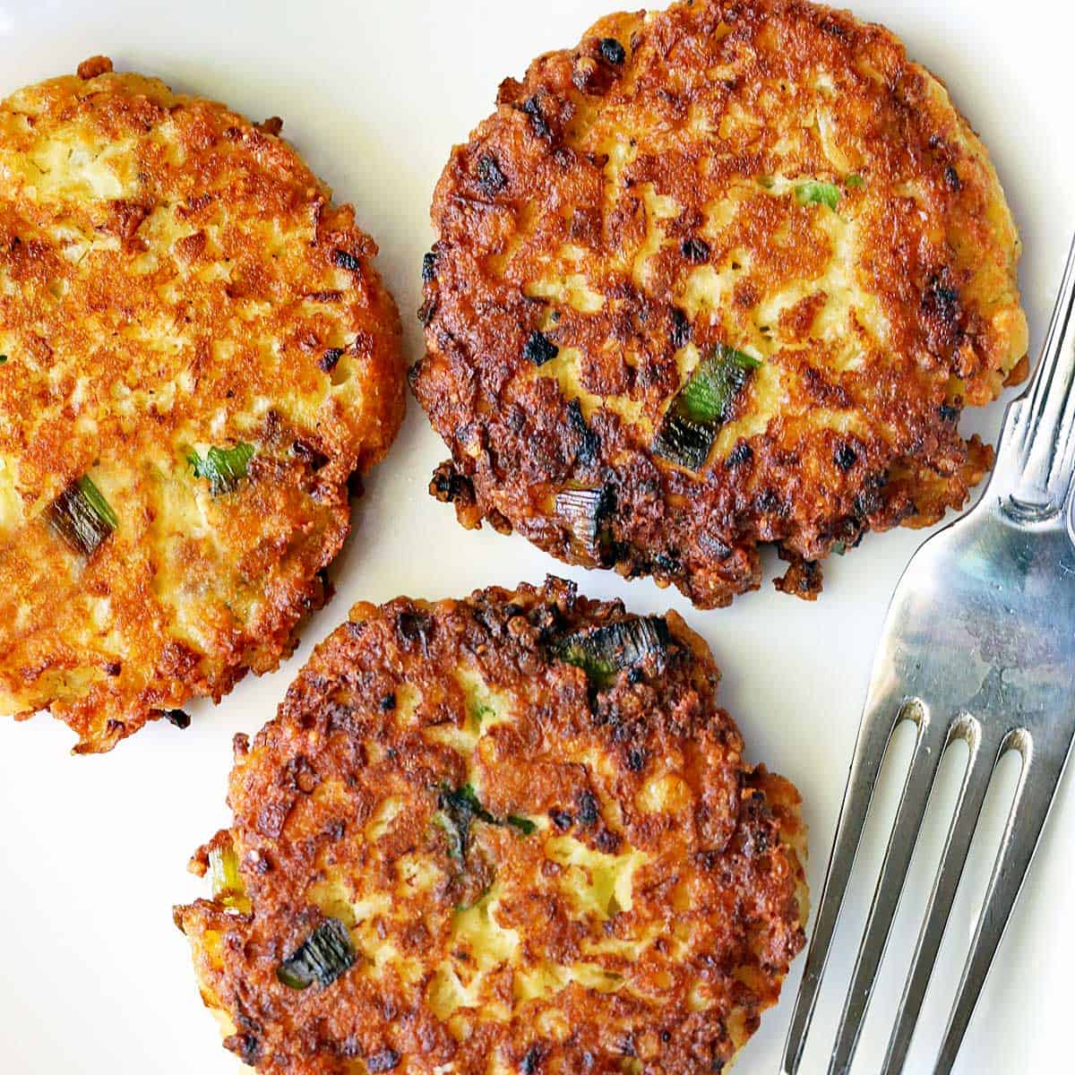 Cauliflower fritters served on a white plate with a fork.