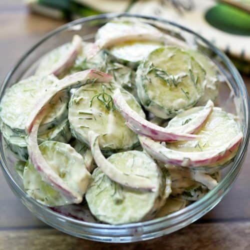 Creamy cucumber salad with sour cream served in a glass bowl.