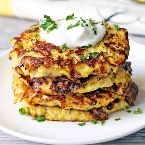 Yellow squash fritters stacked on a white plate.