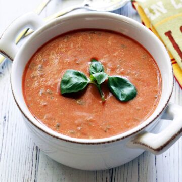 Cold tomato soup garnished with a basil leaf.