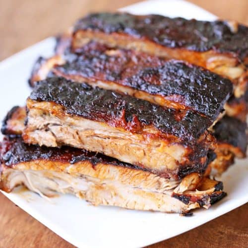 Oven-baked ribs stacked on a white plate.
