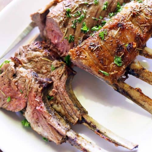 Roasted rack of lamb topped with chopped parsley and served on a white plate.