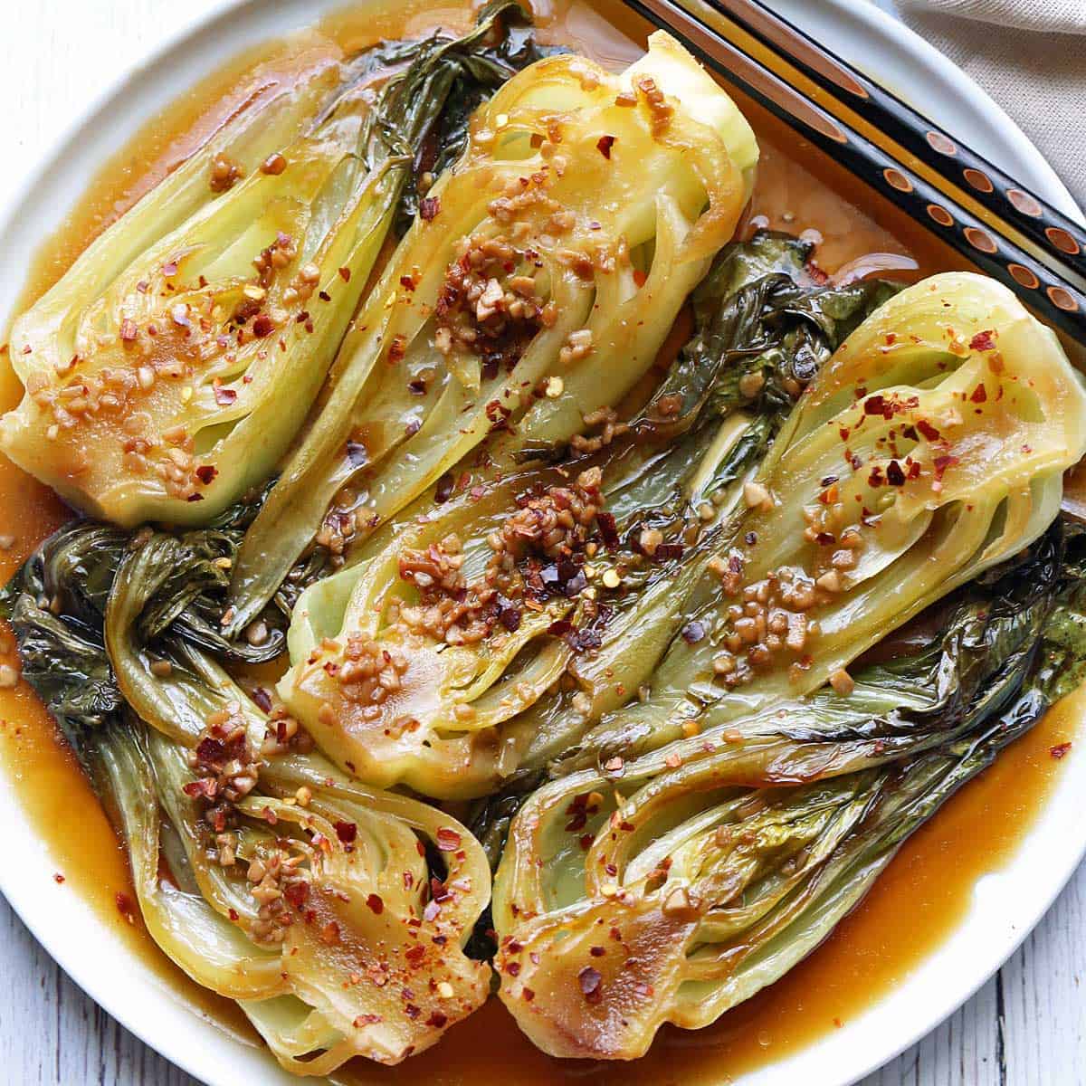 Sauteed bok choy served on a white plate with chopsticks.