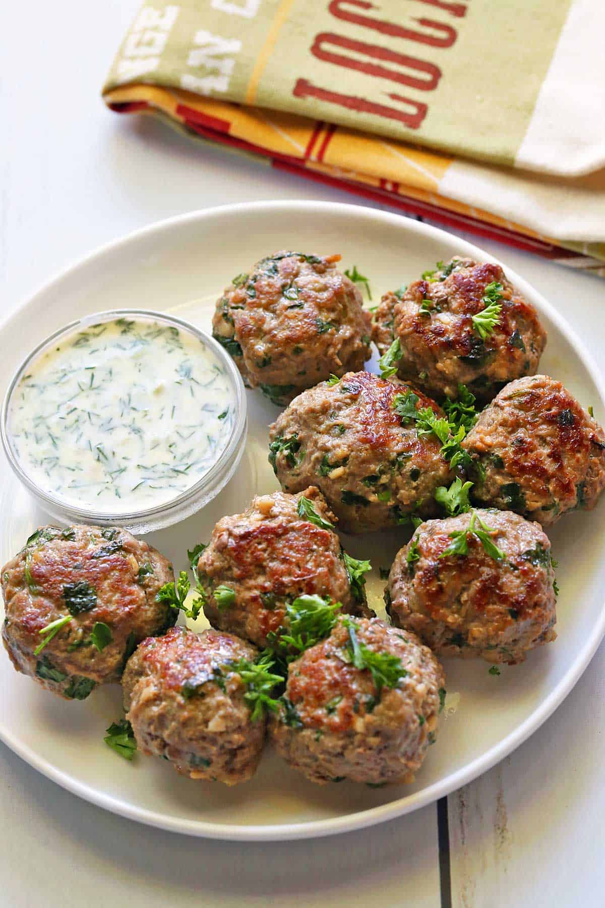 Lamb Meatballs served on a white plate with a dipping sauce. 