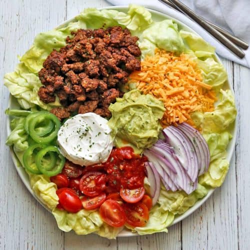 Keto taco salad is served on a white plate with a napkin and silverware.