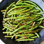 Spicy green beans are served on a dark plate.