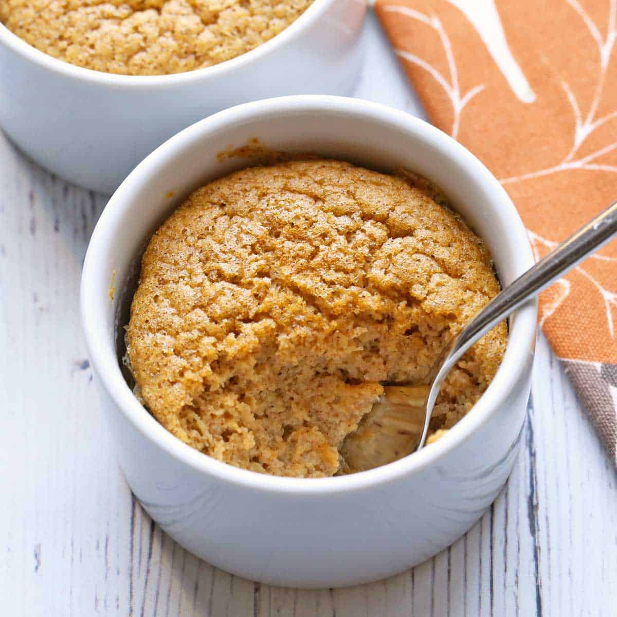 Butternut squash souffle is served in a white ramekin with a spoon.