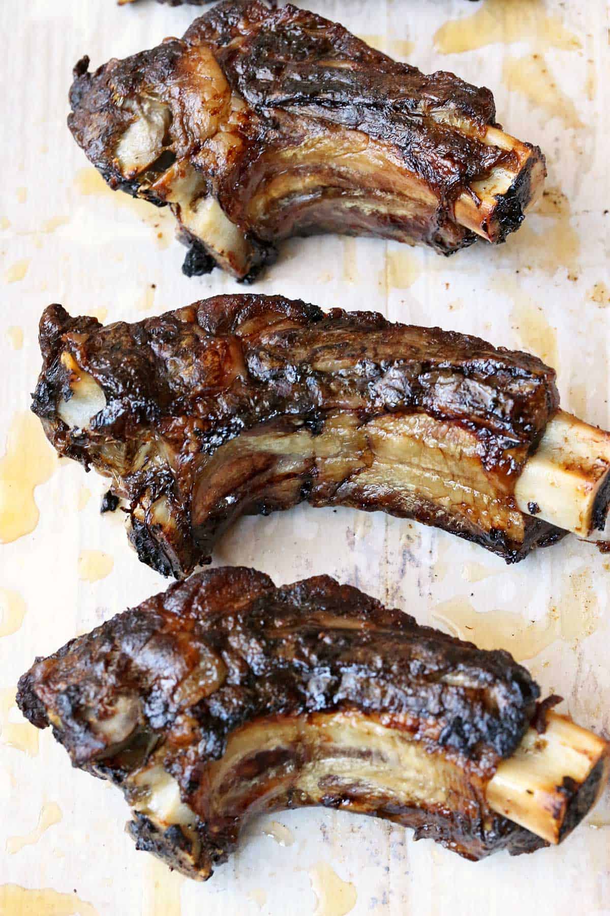 Three beef back ribs, served on a parchment-lined baking sheet. 