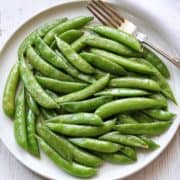 Sauteed sugar snap peas served on a white plate with a fork.