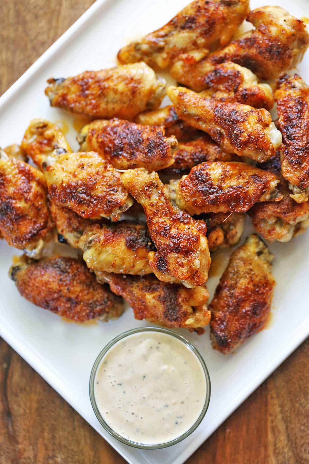 Baked chicken wings are piled on a platter and served with a dipping sauce. 