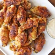 Baked chicken wings are served on a white plate with a dip.