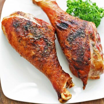 Turkey legs served on a white plate with a garnish of parsley.
