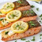 Pan-fried salmon served on a white plate, topped with lemon slices.