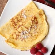 Keto crepes served on a white plate with a garnish of berries.