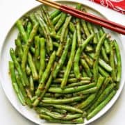 Chinese green beans served on a white plate with chopsticks.