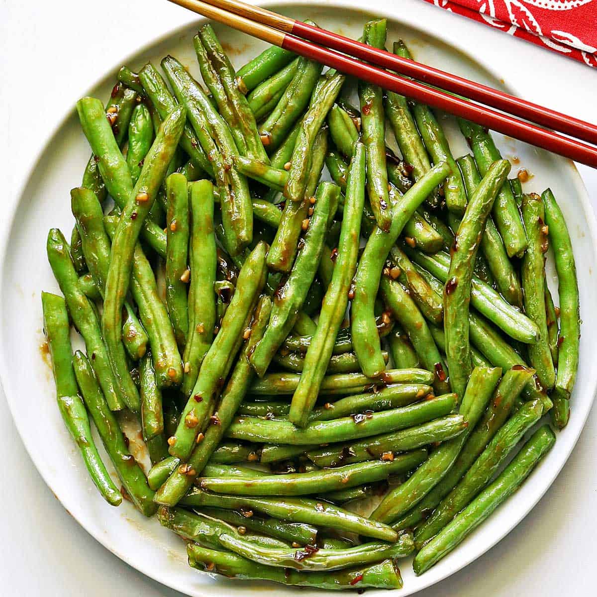 Chinese green beans served on a white plate with chopsticks.