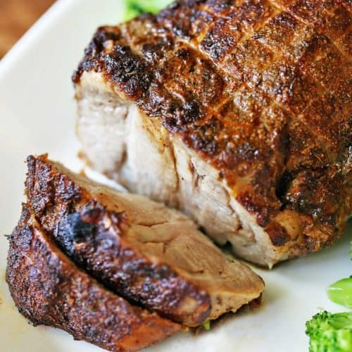 Pork roast, sliced, and served on a white platter with broccoli.