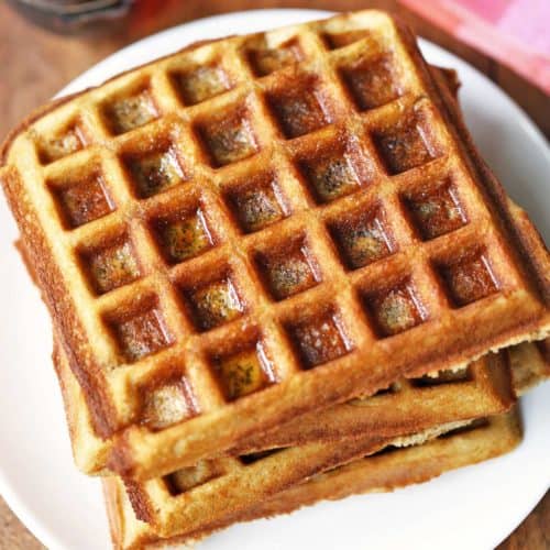 Keto almond flour waffles stacked on a white plate.
