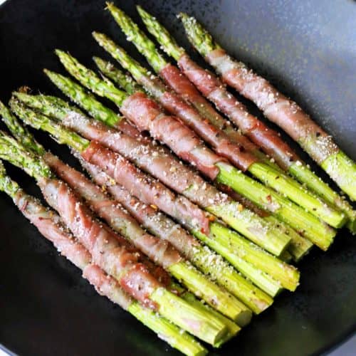 Prosciutto-wrapped asparagus served on a dark plate.