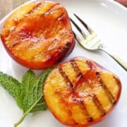 Grilled peaches served on a white plate with a fork.