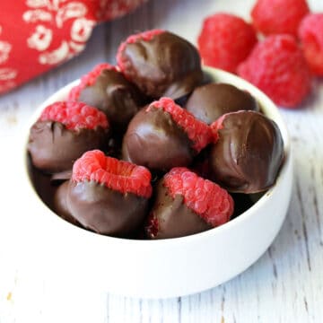 Chocolate-covered raspberries served in a white bowl.