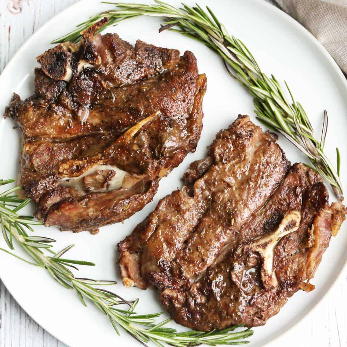 Lamb shoulder chops served on a white plate with a garnish of rosemary.