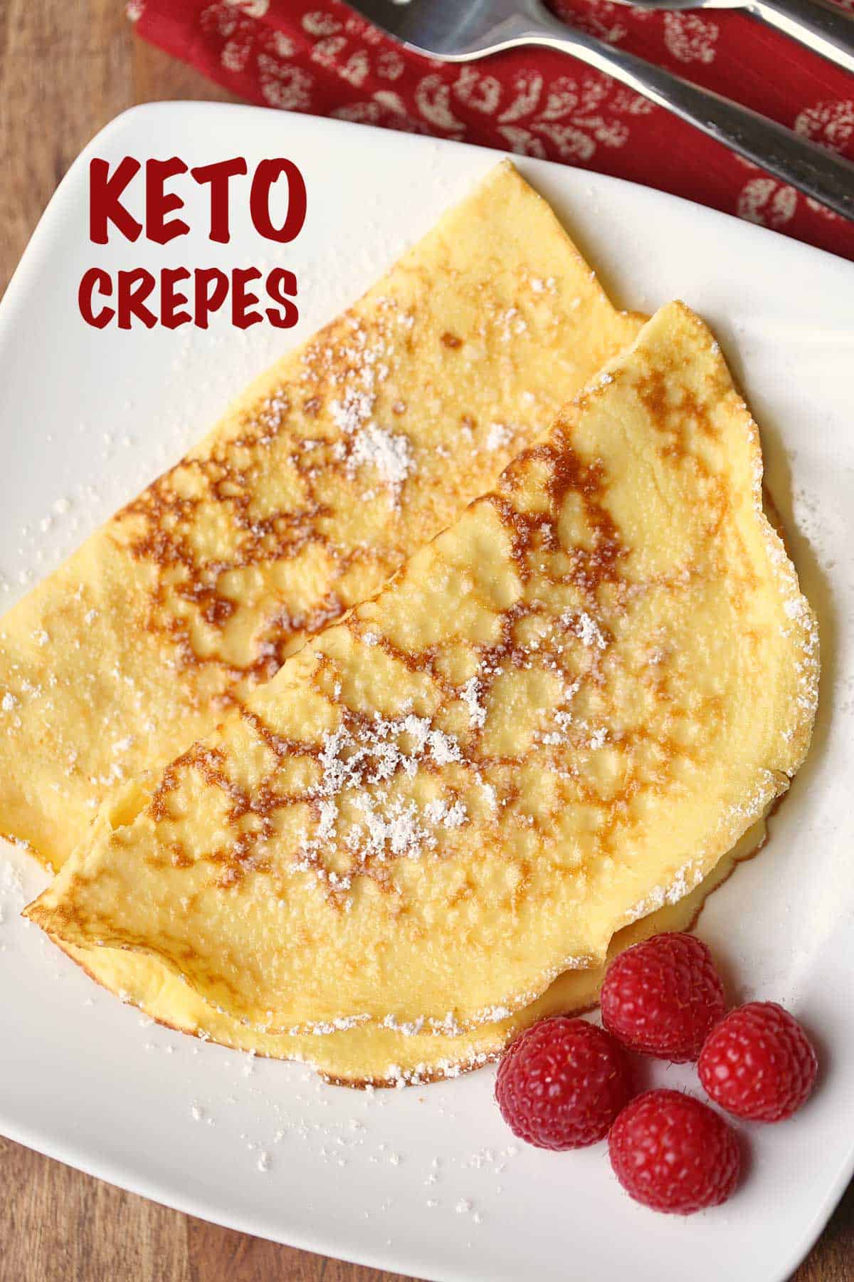 Two keto crepes served on a white plate garnished with raspberries. 