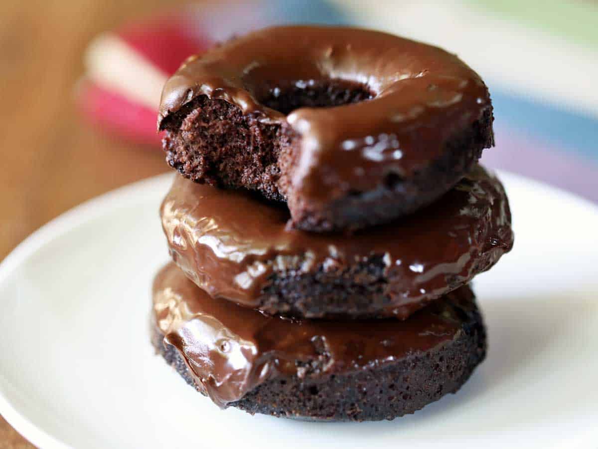 Three chocolate-glazed keto donuts stacked on a white plate.