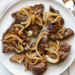 Liver and onions are served on a white plate with utensils.