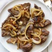 Liver and onions served on a white plate with utensils.