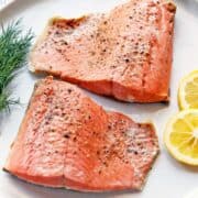 Poached salmon served on a white plate with lemon slices.