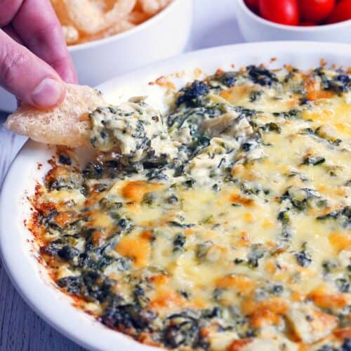 A hand scooping up some spinach artichoke dip.