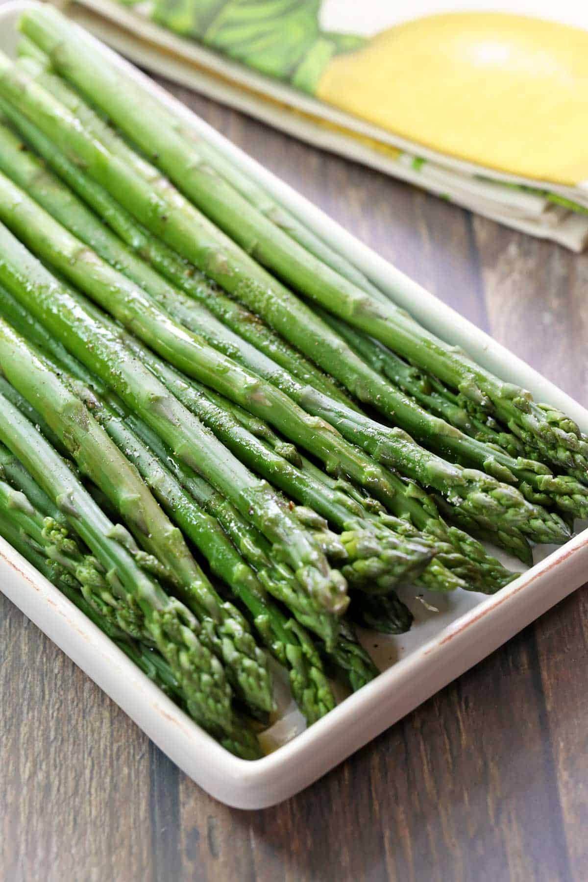 Steamed asparagus served on a white platter with a napkin. 