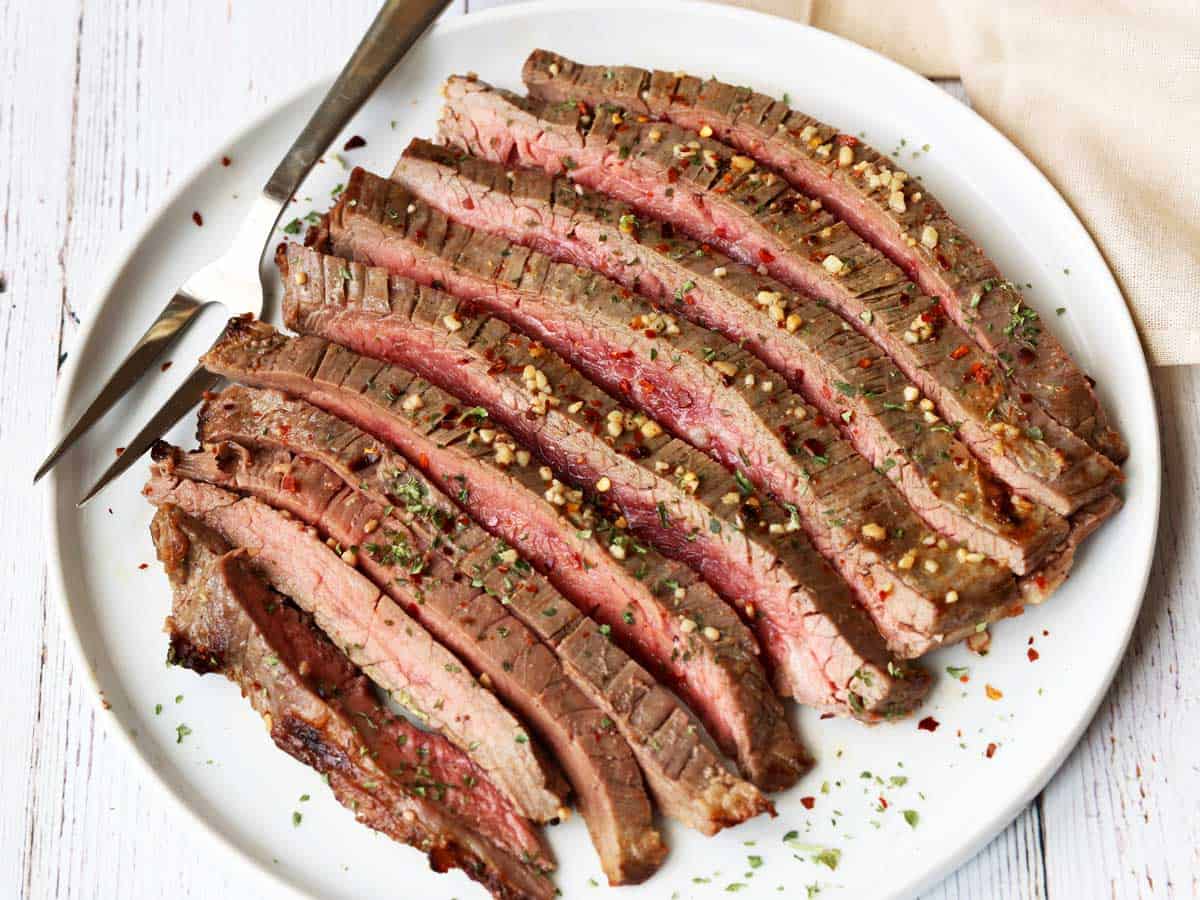 Broiled flank steak, sliced and served on a white plate. 