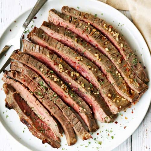 Broiled flank steak, sliced, served on a white plate.