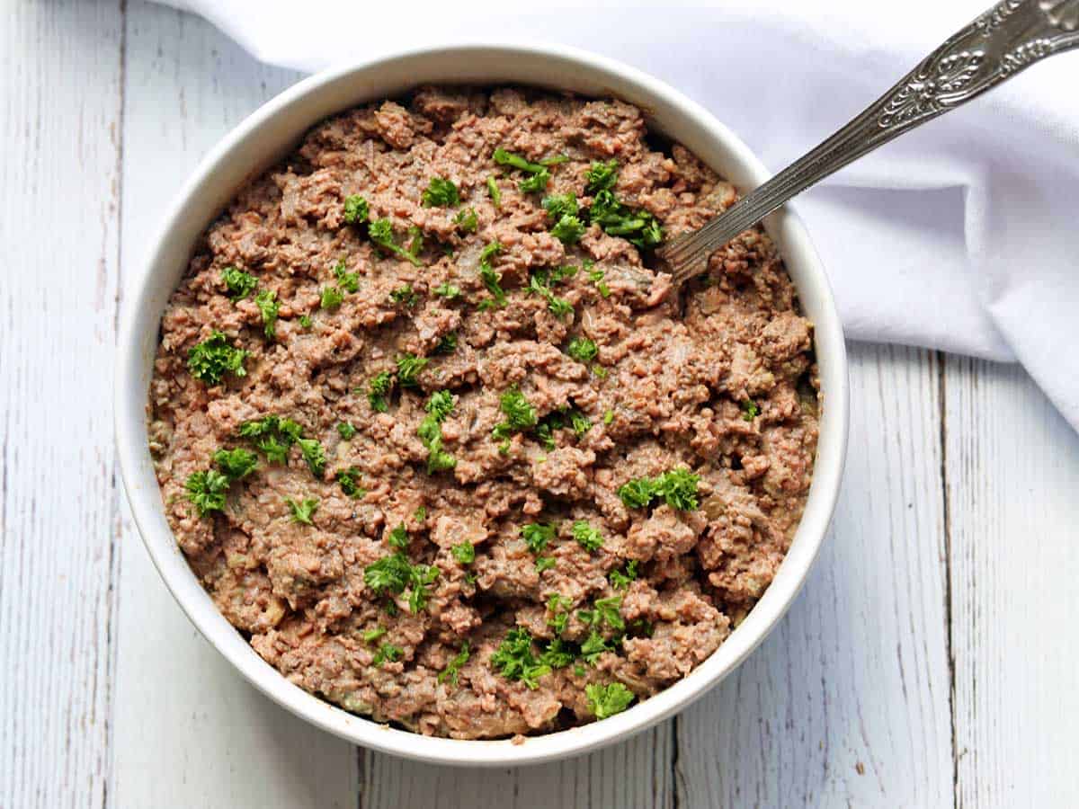 Chopped liver is served in a white bowl with a spoon. 