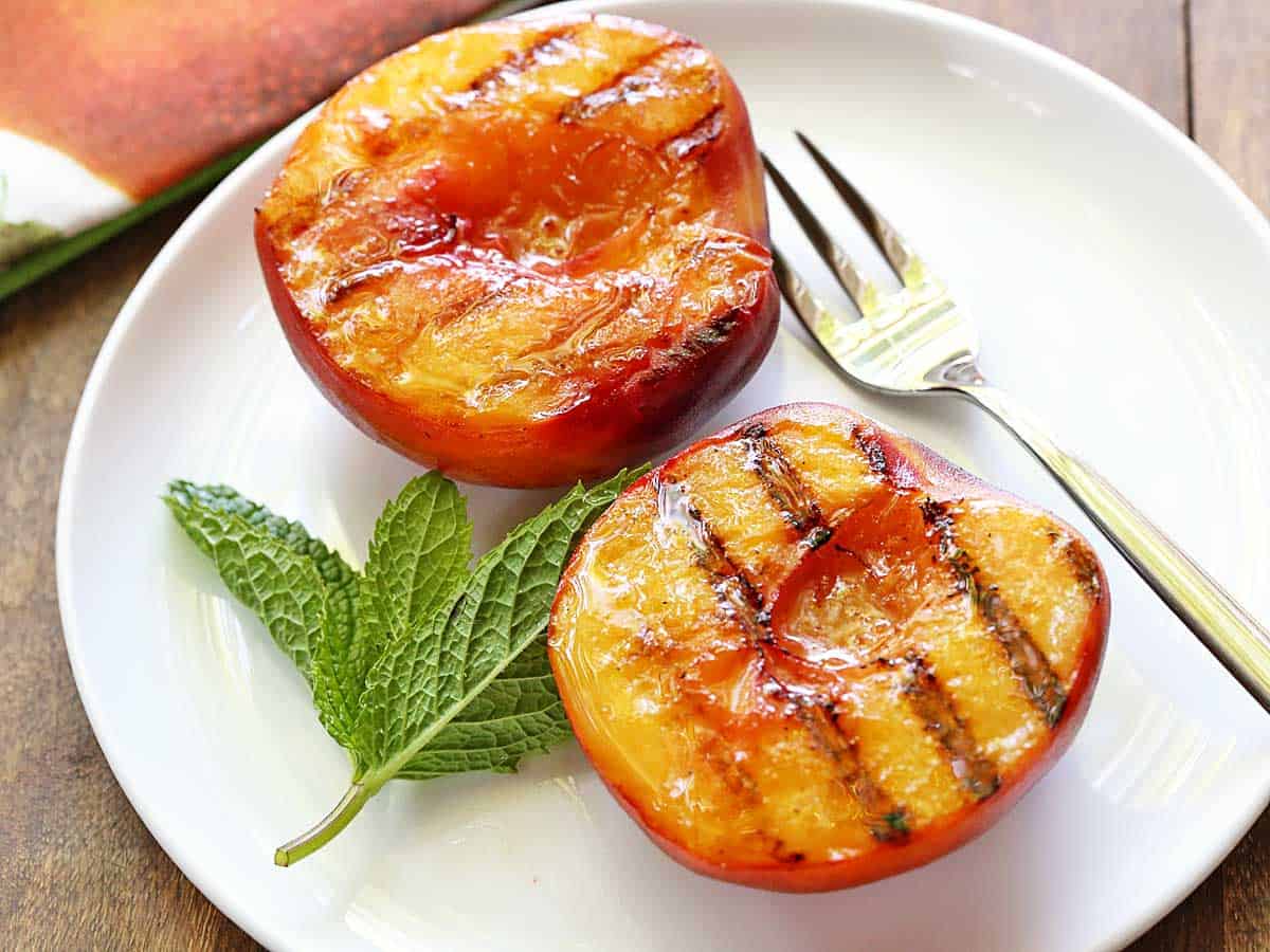 Grilled peaches served on a white plate with a fork. 