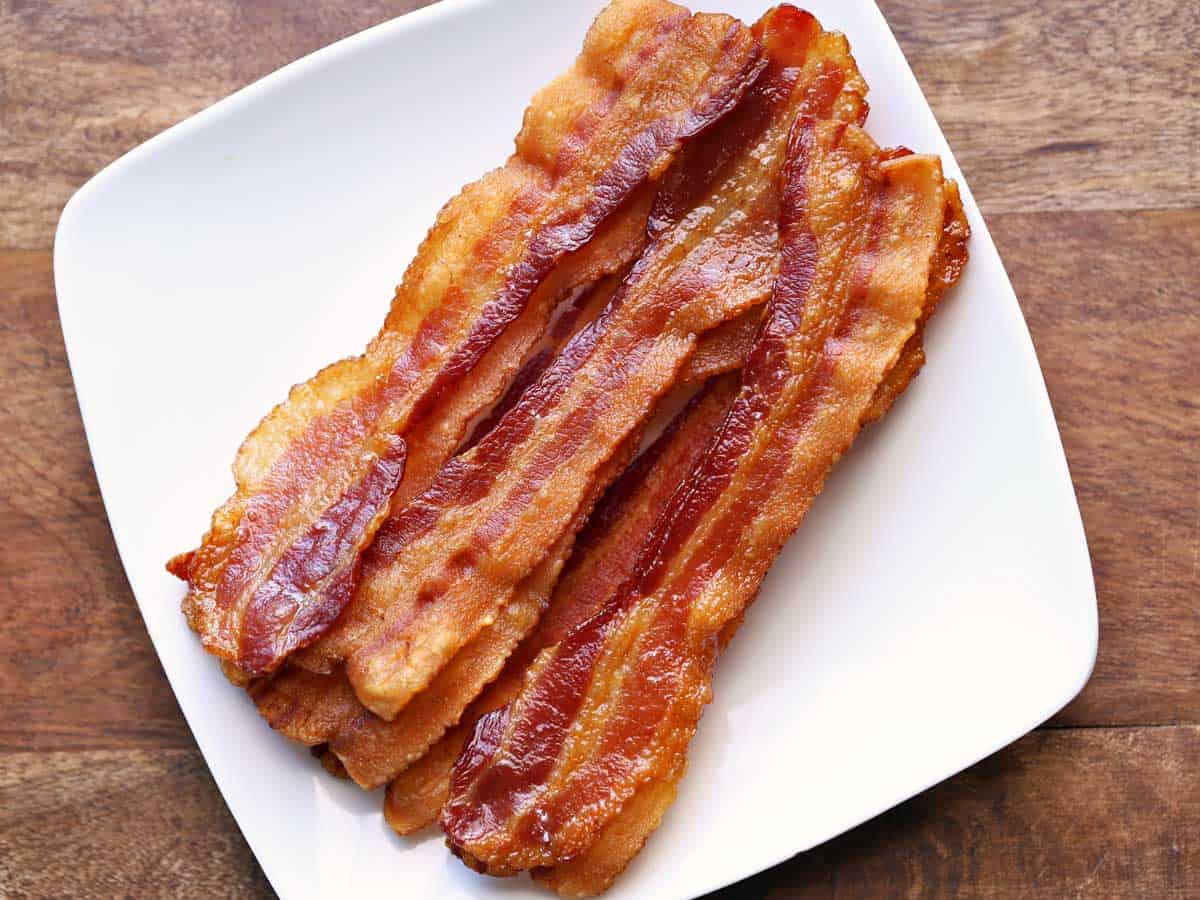 Strips of oven-baked bacon piled on a white plate.