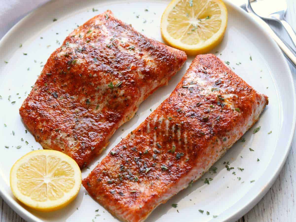 Paprika salmon served on a plate with slices of lemon. 