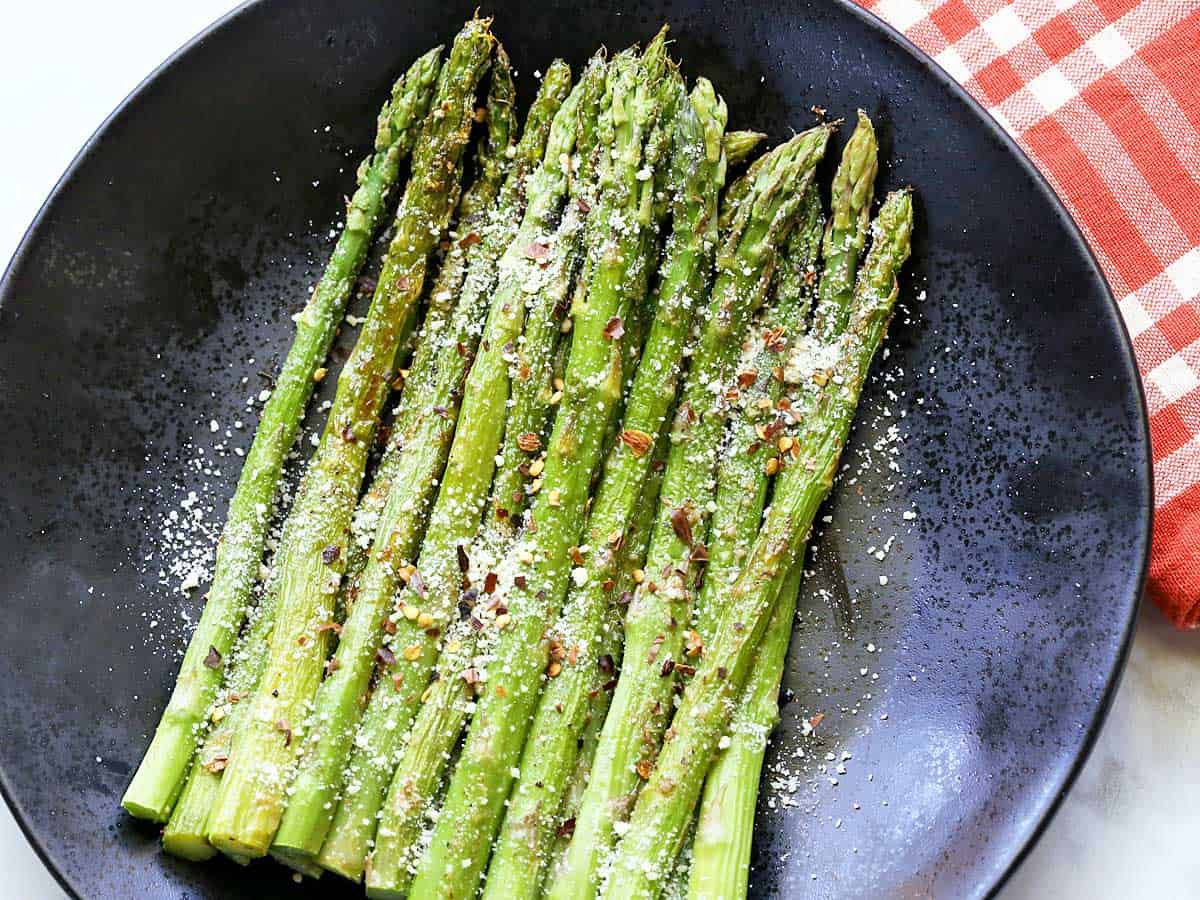 Roasted asparagus spears served on a black plate, topped with grated parmesan. 
