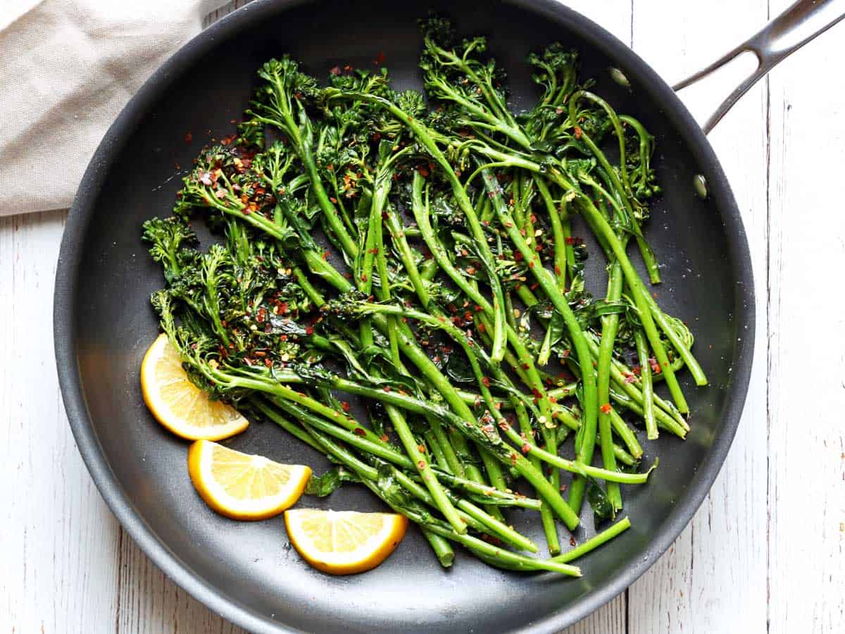 Sauteed broccolini in a skillet with lemon slices. 