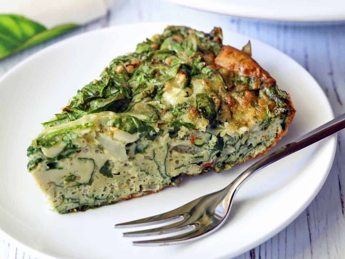 A slice of spinach frittata served on a white plate with a fork.